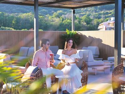 Dos personas descansan bajo una pérgola en una terraza con vistas a la montaña.