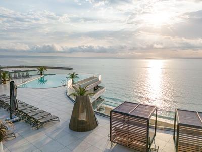 Terraza de lujo con piscina infinita y áreas de descanso con vistas al mar al atardecer.