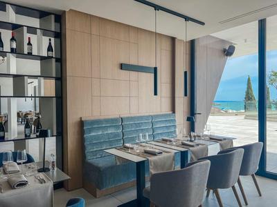 Modern dining area with blue chairs and bench seating next to large windows overlooking the sea.