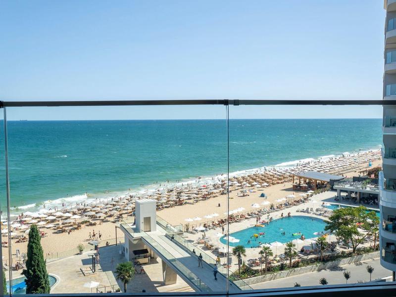 Widok na plażę z parasolami i basenem obok budynku hotelu.