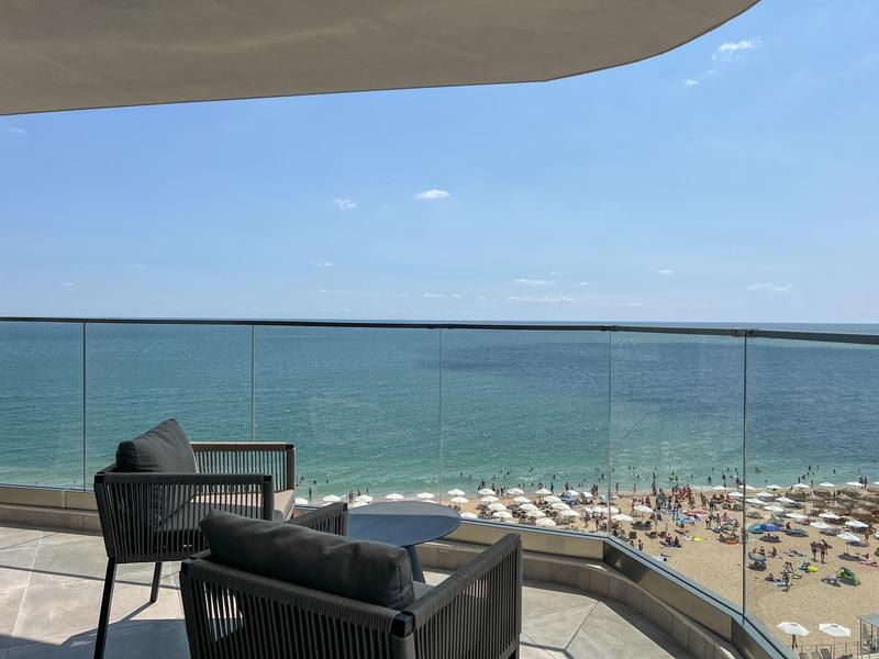 Balkon z dwoma krzesłami z widokiem na plażę z parasolami i morze.