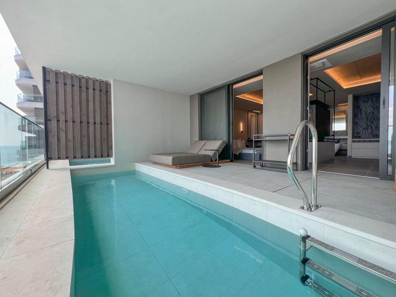 Nowoczesny balkon z długim basenem, leżakami i szklaną balustradą w pokoju hotelowym.