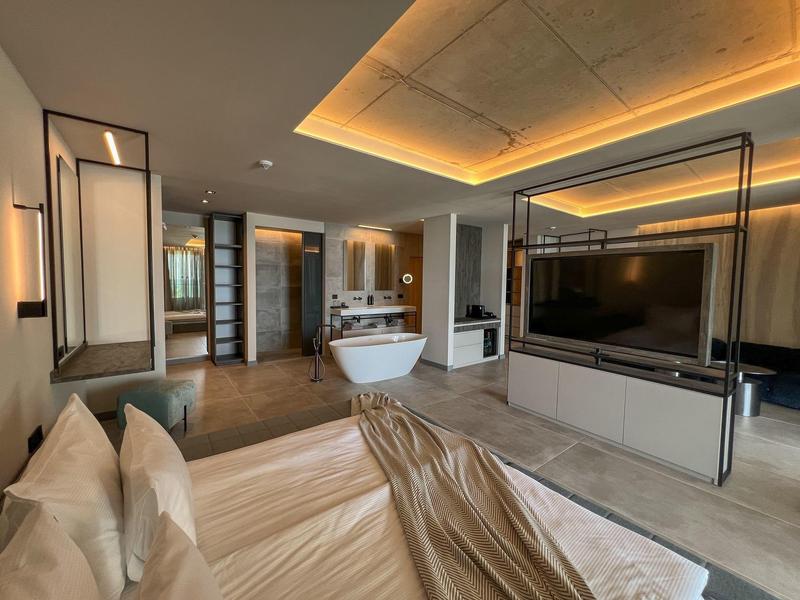 Nowoczesny pokój hotelowy z otwartą łazienką, wolnostojącą wanną i dużym telewizorem.