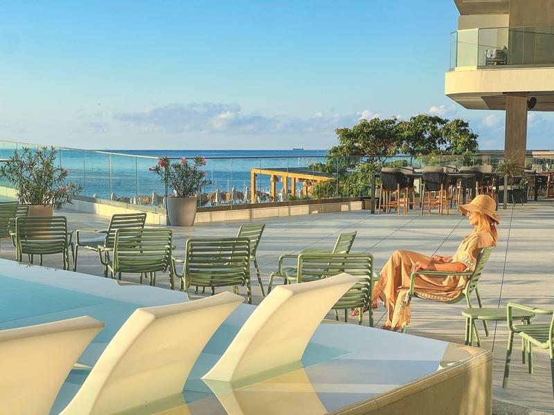 Kobieta relaksująca się przy basenie z widokiem na morze i taras hotelowy.