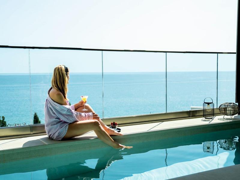 Kobieta siedzi na brzegu basenu z widokiem na morze pod czystym niebem.