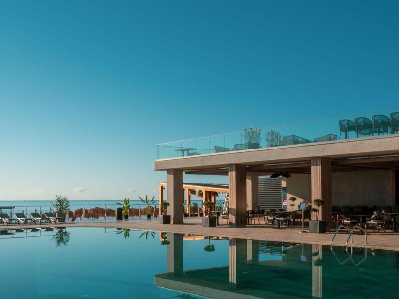 Nowoczesny basen hotelowy z tarasem słonecznym i widokiem na czyste niebieskie niebo.