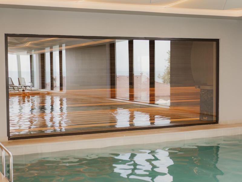 Widok na kryty basen z dużym oknem wychodzącym na przylegający drewniany podest.