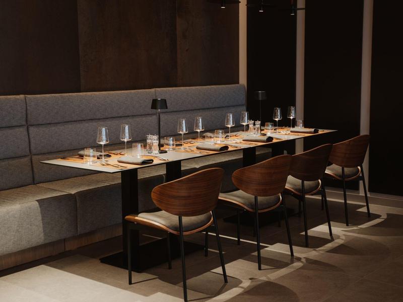 Elegancka jadalnia z drewnianymi stołami, nowoczesnymi krzesłami i przyciemnionym oświetleniem.