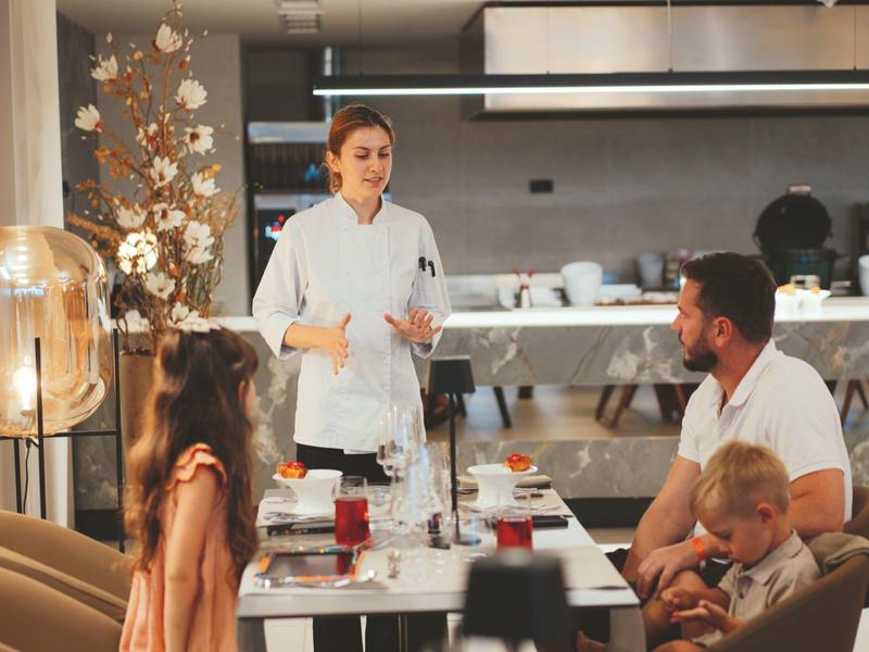 Kelnerka rozmawia z rodziną przy nakrytym stole w nowoczesnej restauracji.