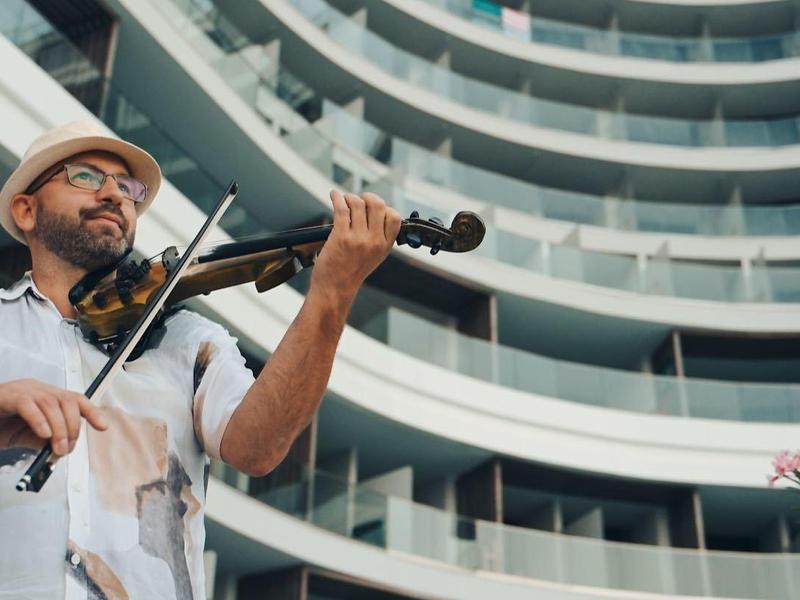 Mężczyzna grający na skrzypcach na zewnątrz przed nowoczesnym, zakrzywionym hotelem.