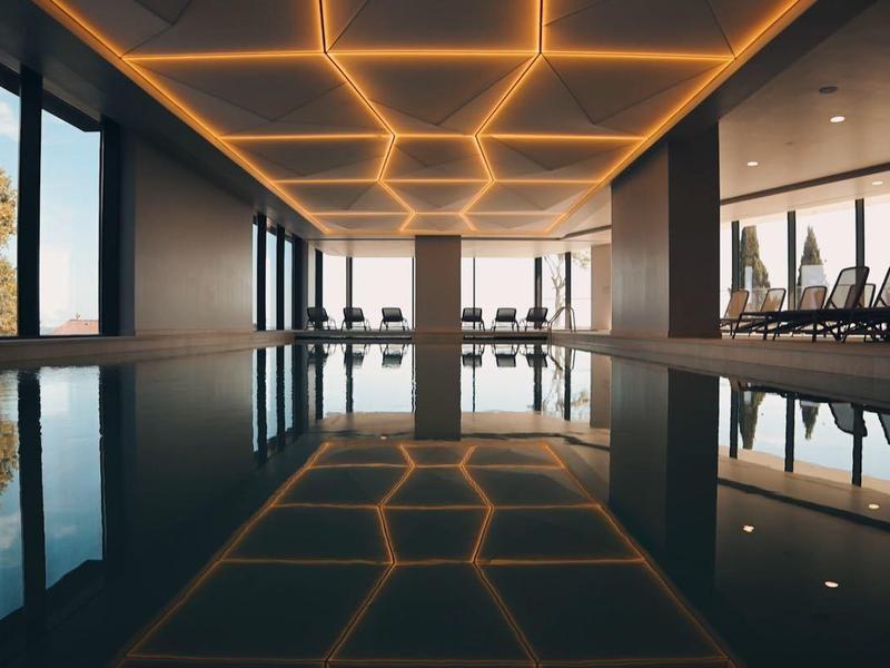 Nowoczesny kryty basen z dużymi oknami i ciepłym oświetleniem sufitowym w hotelu.