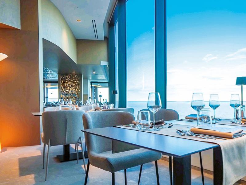 Nowoczesna restauracja z dużymi oknami, nakrytymi stolikami i jasnym światłem dziennym.