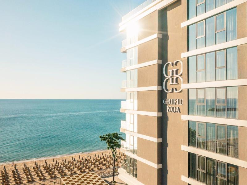 Wysoki budynek przy plaży z widokiem na morze i parasolki na piaszczystym brzegu.