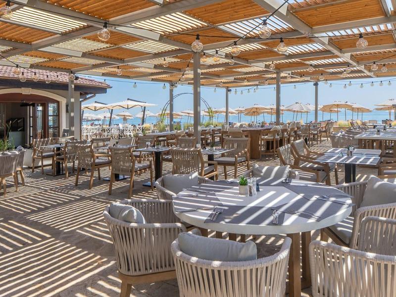 Zadaszony taras na zewnątrz z wieloma stołami i krzesłami w hotelu lub restauracji.