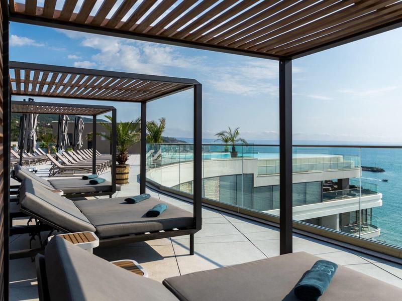Luksusowe leżaki na tarasie z widokiem na morze i szklaną balustradą pod niebieskim niebem.