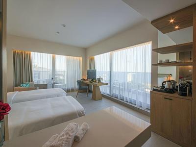 Helles Hotelzimmer mit zwei Betten, großen Fenstern, Schreibtisch und offenem Regal mit Kaffeemaschine.