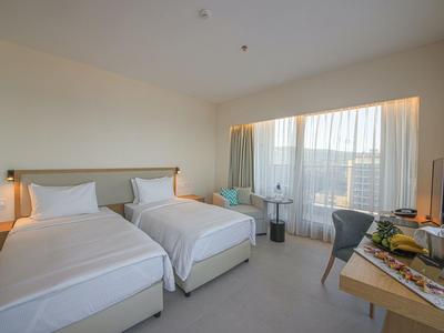 Helles Hotelzimmer mit zwei Einzelbetten, Schreibtisch, Stuhl und großem Fenster mit Vorhängen.