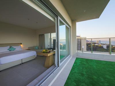 Modernes Hotelzimmer mit großem Bett, Glastür und Balkon mit grünem Kunstrasen.