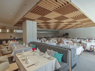 Großer Restaurantraum mit weißen Tischdecken, bequemen Stühlen und Holzdecke mit dekorativen Lamellen.