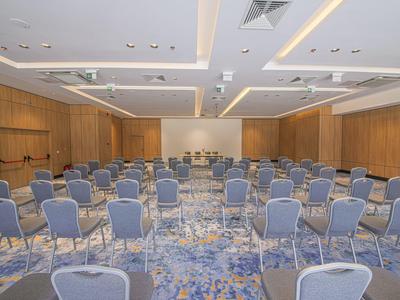 Großer Konferenzraum mit blauen Stühlen, Holzpanelen und hellem, beleuchtetem Deckensystem.