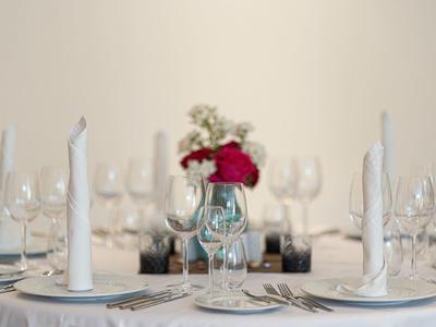 Eleganter Esstisch mit weißen Kerzen, Gläsern, Besteck und rotem Blumenstrauß in der Mitte.