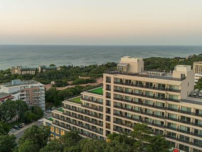 Große Wohnhäuser am Meer mit vielen Balkonen, umgeben von grünen Bäumen und weiter Aussicht aufs Wasser.