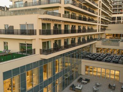 Moderne mehrstöckige Wohnanlage mit Balkonen, Glasfassade und Terrasse mit Sitzplätzen bei Abendlicht.