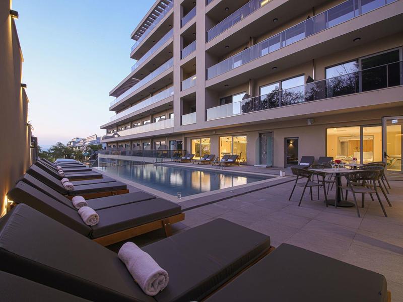 Moderner Außenpoolbereich mit Liegestühlen, Handtüchern und beleuchtetem Essbereich am Abend.