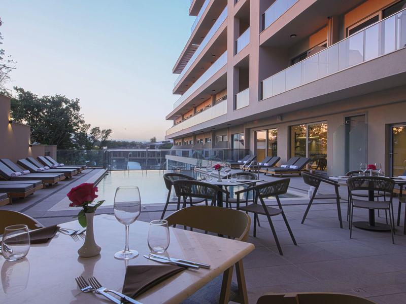 Moderne Hotelterrasse mit Glasgeländer, Sonnenliegen und Pool bei Sonnenuntergang.