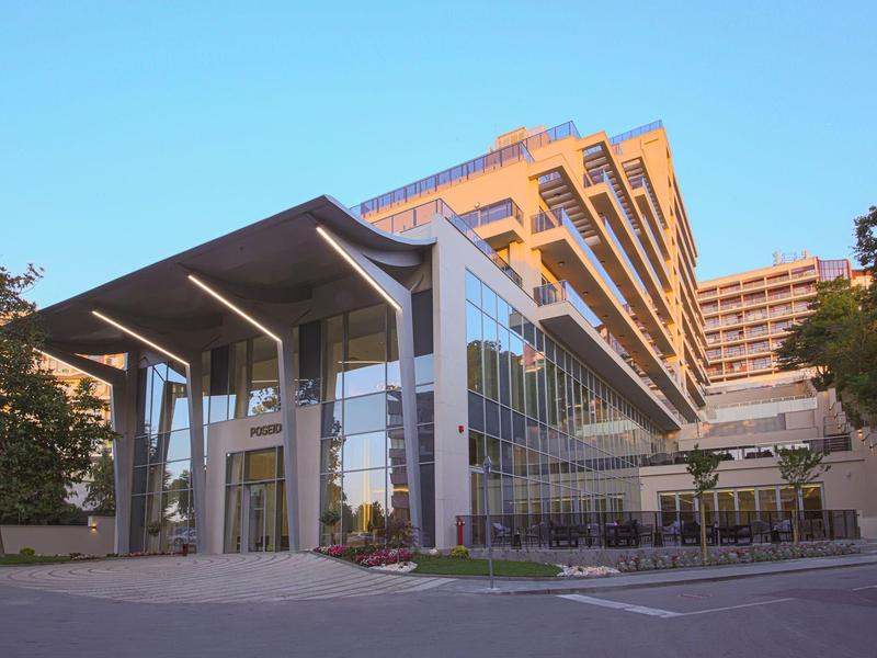 Modernes Gebäude mit Glasfassade, überdachtem Eingang und mehrstöckigem Anbau im Abendlicht.