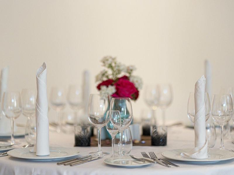 Eleganter Esstisch mit weißen Kerzen, Gläsern, Besteck und rotem Blumenstrauß in der Mitte.