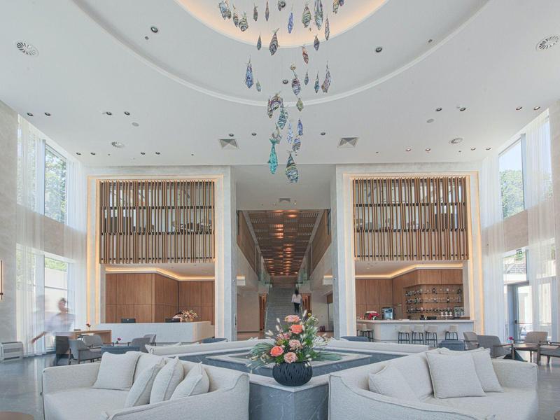 Großer, heller Wohnbereich mit hohen Decken, Sofas, Blumenarrangement und moderner Deckenbeleuchtung.