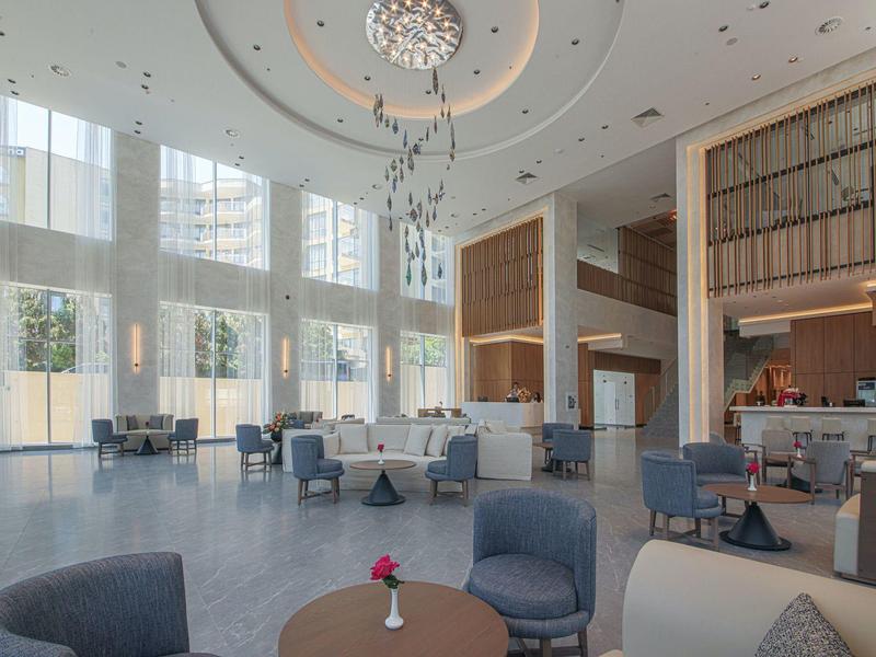 Großer moderner Lounge-Bereich mit hohen Fenstern, blauen Sesseln und Kronleuchter an der Decke.