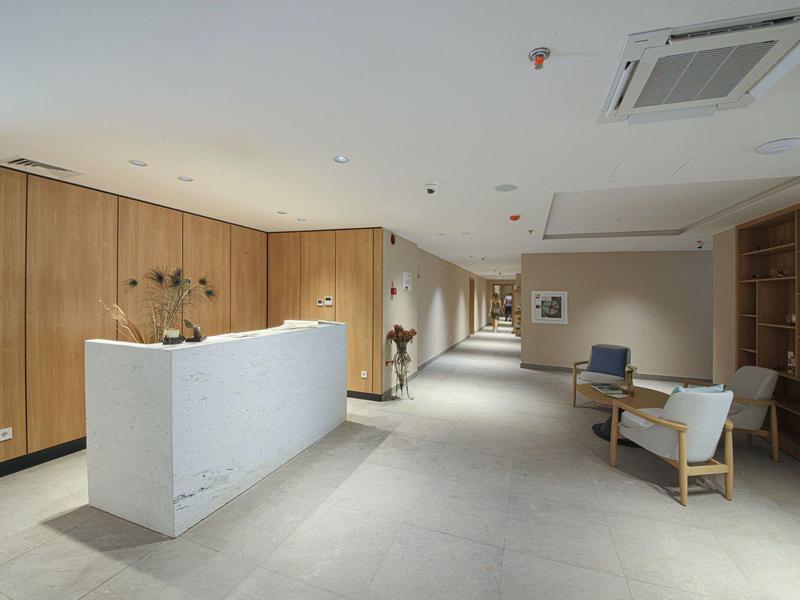 Moderner Empfangsbereich mit weißer Rezeption, Holzwänden und Sitzbereich mit Stühlen und Laptop.