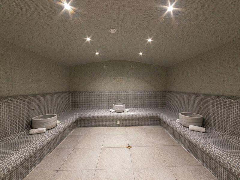 Moderner Dampfraum mit grauen Fliesen, Sitzbänken und Deckenbeleuchtung.