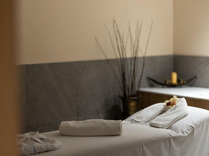 Weiß gedeckte Massageliege mit Rolletuch in ruhigem, minimalistischem Behandlungsraum.