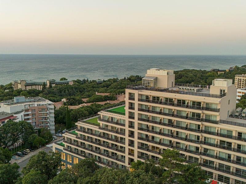 Große Wohnhäuser am Meer mit vielen Balkonen, umgeben von grünen Bäumen und weiter Aussicht aufs Wasser.
