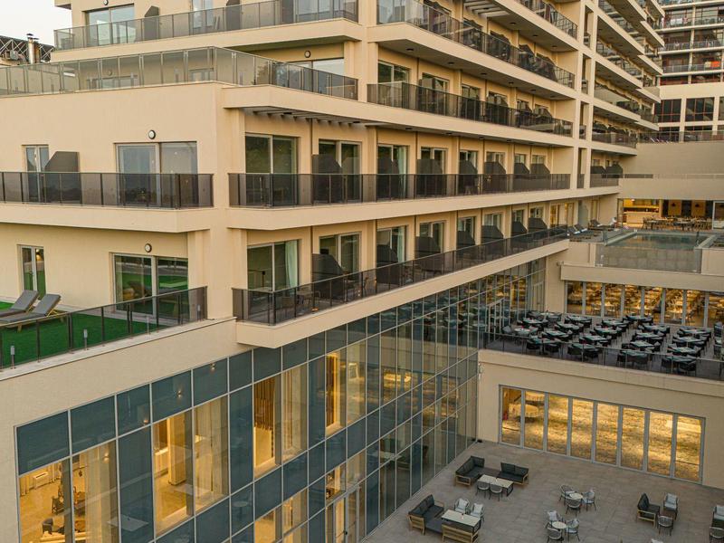 Moderne mehrstöckige Wohnanlage mit Balkonen, Glasfassade und Terrasse mit Sitzplätzen bei Abendlicht.