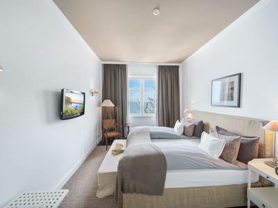 Camera d'hotel moderna e luminosa con due letti, TV e grande finestra con tende.