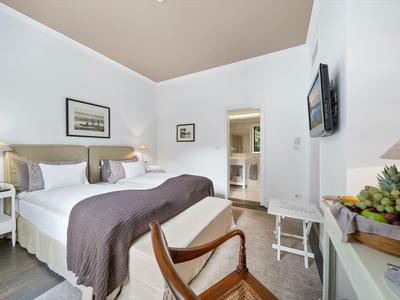 Camera d'hotel luminosa con letti grandi, sedia, TV e arredamento moderno.