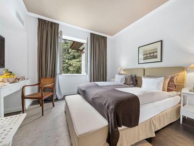 Camera d'hotel accogliente con letto matrimoniale, scrivania, sedia e finestra con vista sugli alberi.