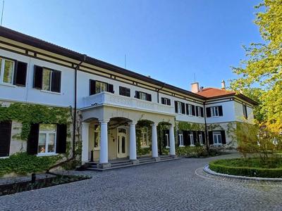 Grande edificio dell'hotel bianco con persiane verdi e cortile lastricato sotto un cielo blu.