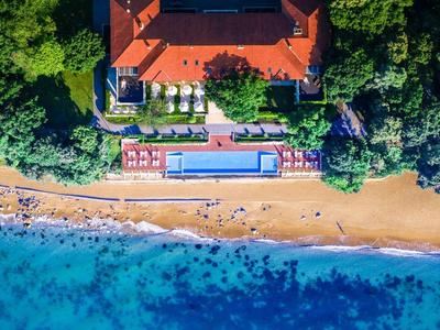 Veduta aerea di un hotel con piscina, circondato da foresta e adiacente a una spiaggia sabbiosa.