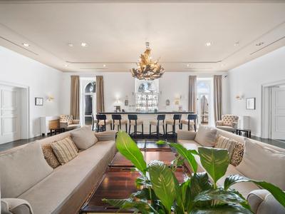 Großes Wohnzimmer mit zwei grauen Sofas, Holz-Tisch, Kronleuchter und grüner Pflanze im Vordergrund.