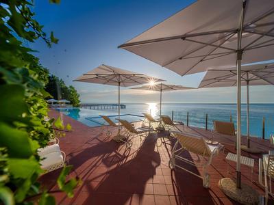 Terrasse mit Liegestühlen und Sonnenschirmen mit Blick auf das Meer bei Sonnenuntergang.