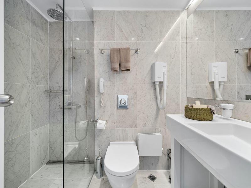 Bagno moderno con doccia walk-in, WC e lavabo in tonalità neutre.