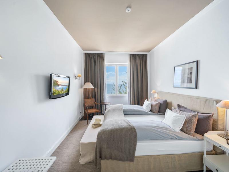 Camera d'hotel moderna e luminosa con due letti, TV e grande finestra con tende.