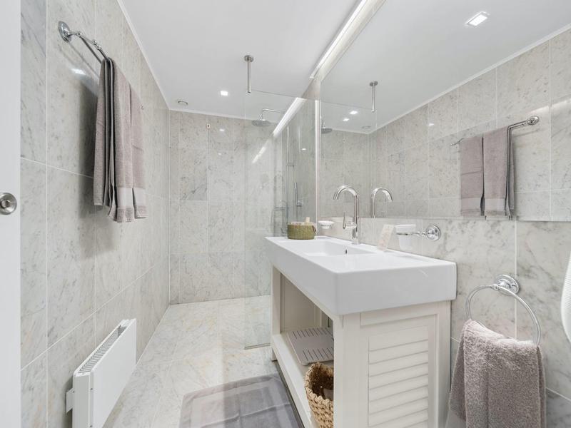 Bagno moderno con grande specchio, lavandini bianchi e asciugamani grigi.