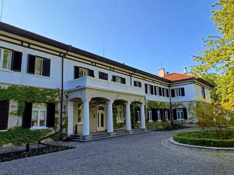 Grande edificio dell'hotel bianco con persiane verdi e cortile lastricato sotto un cielo blu.