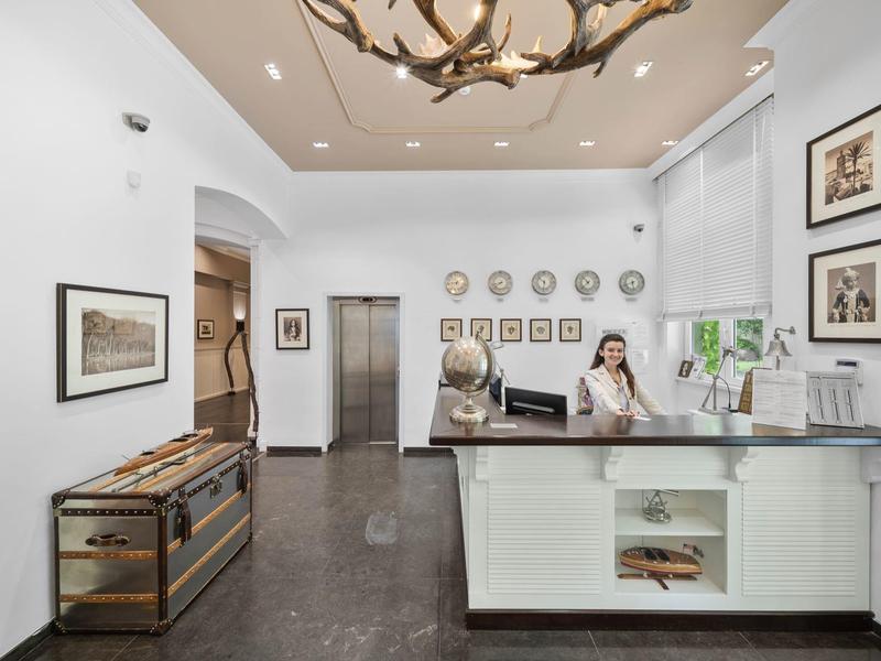 Reception con bancone chiaro e due dipendenti in ambiente alberghiero elegante.